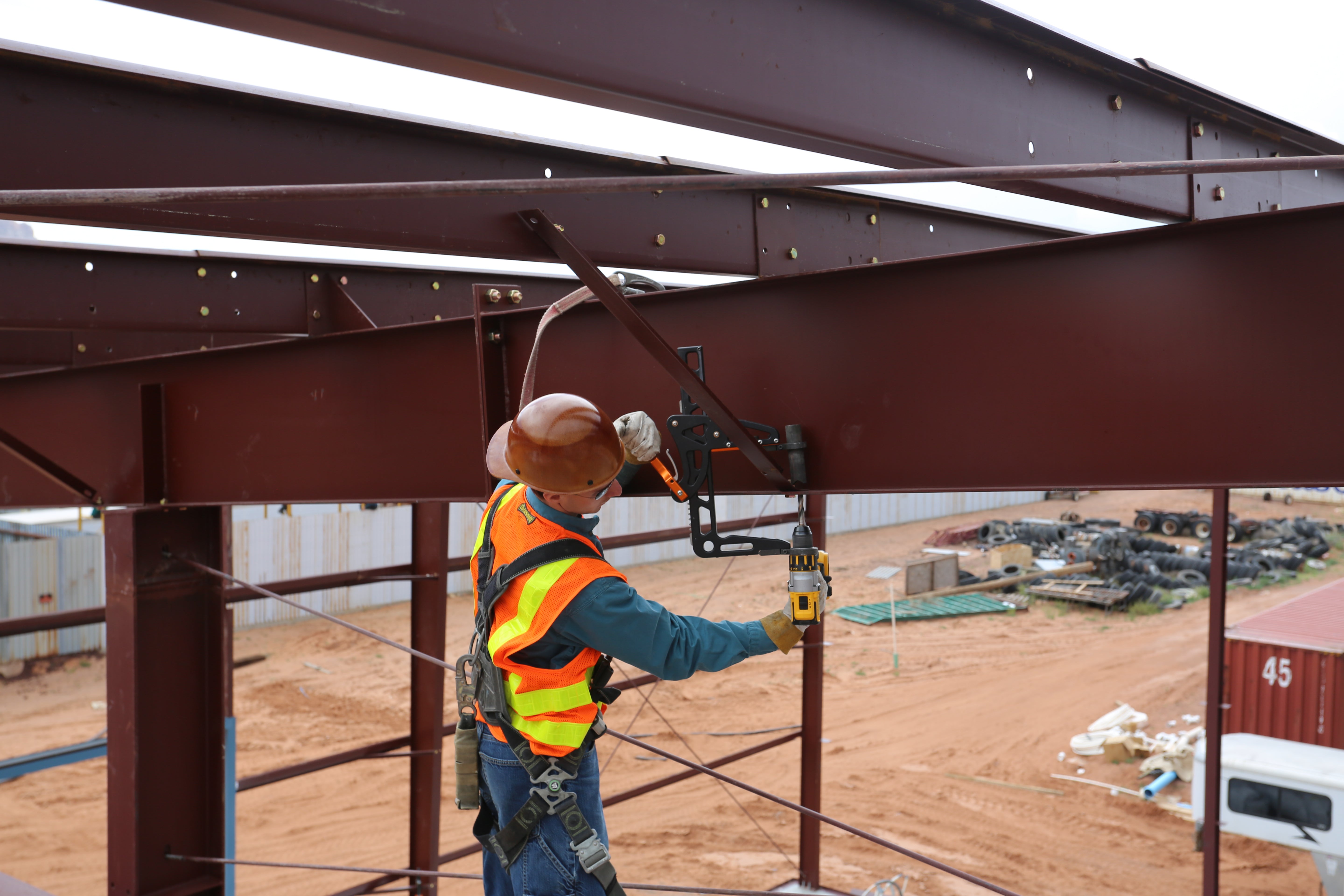 Construction worker at a jobsite drilling through a beam overhead with a rapidrill attachment